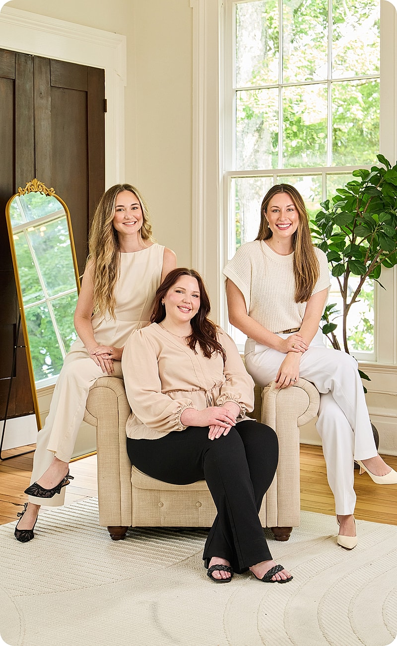 Three women posing together in a bright room.