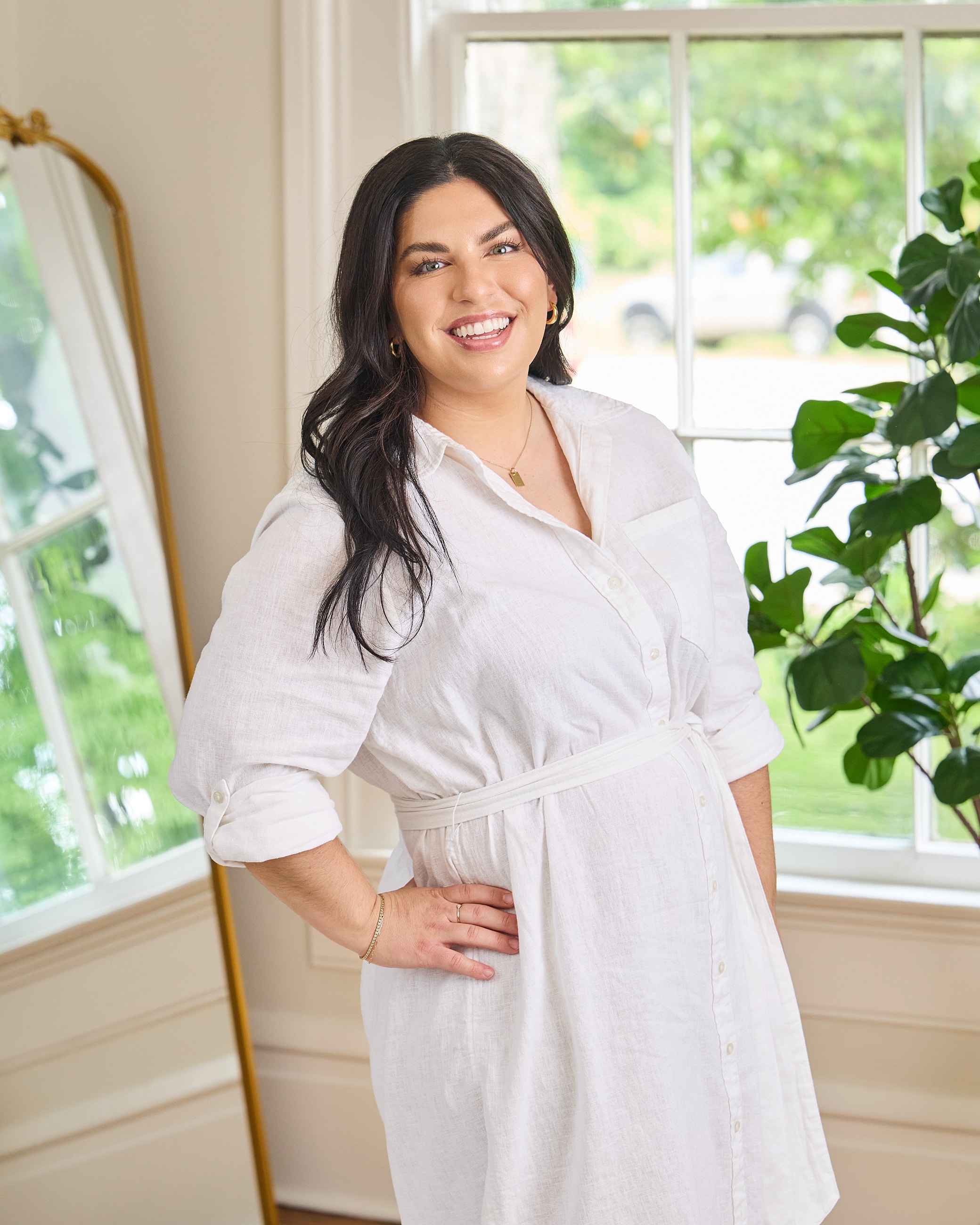 Smiling woman in white dress by window.